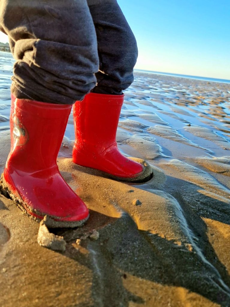 un enfant portant des bottes sur la plage à marée basse